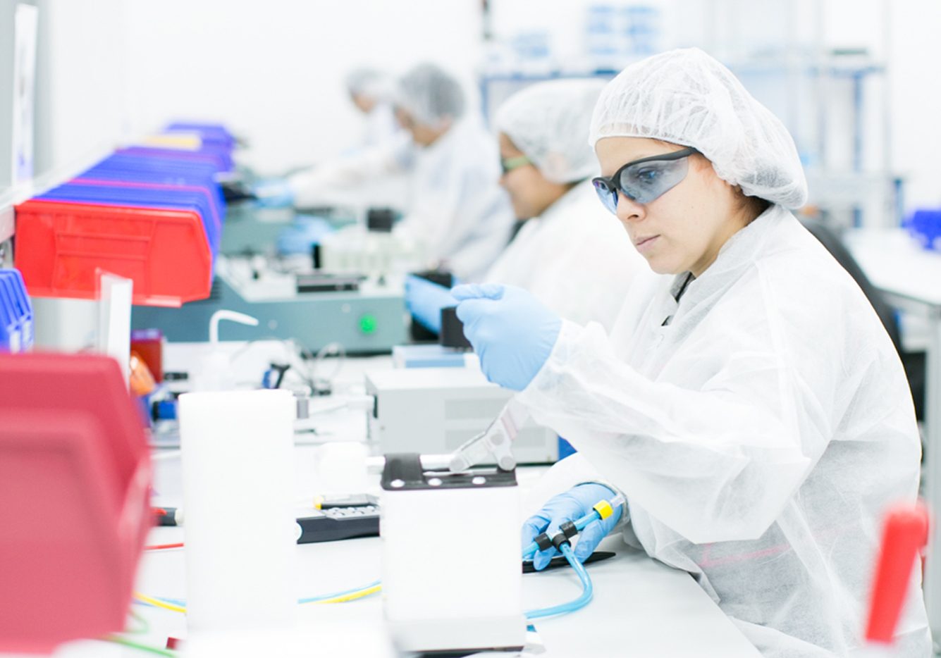 A team of lab technicians in cleanroom garments working meticulously with laboratory equipment in a high-tech contract manufacturing facility.